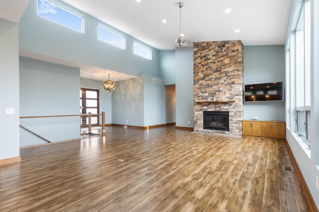 unfurnished living room with a chandelier, wood-type flooring, high vaulted ceiling, and a stone fireplace