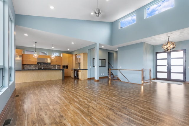 unfurnished living room with french doors, high vaulted ceiling, a healthy amount of sunlight, and hardwood / wood-style flooring