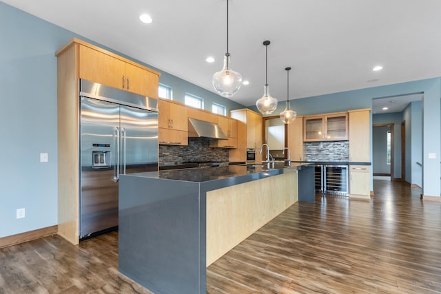 kitchen featuring backsplash, built in refrigerator, a center island with sink, and extractor fan