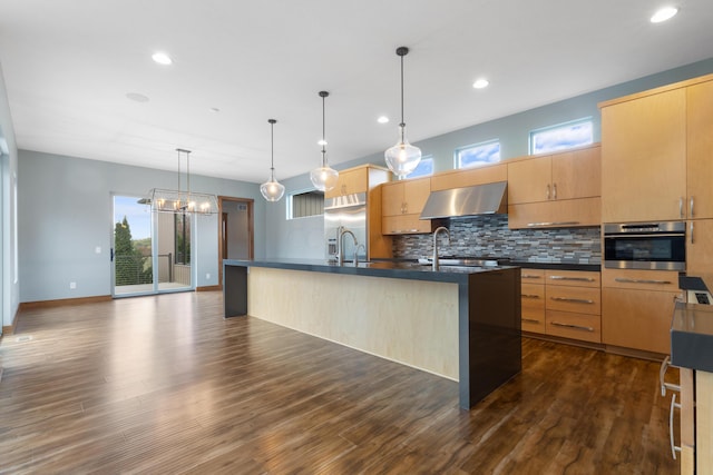 kitchen featuring appliances with stainless steel finishes, ventilation hood, a kitchen island with sink, dark hardwood / wood-style floors, and hanging light fixtures