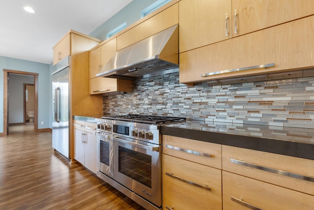 kitchen featuring light brown cabinets, dark wood-type flooring, premium appliances, tasteful backsplash, and range hood