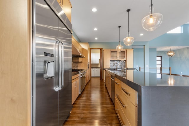 kitchen with hanging light fixtures, premium appliances, tasteful backsplash, dark hardwood / wood-style floors, and a center island with sink