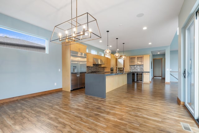 kitchen with exhaust hood, built in fridge, light wood-type flooring, tasteful backsplash, and decorative light fixtures