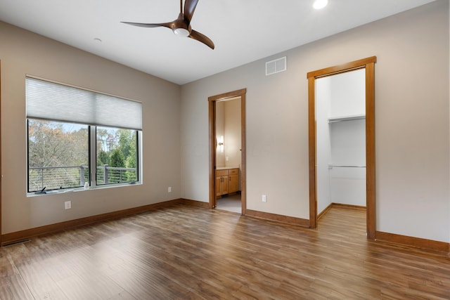 unfurnished bedroom with ensuite bathroom, a walk in closet, light hardwood / wood-style flooring, ceiling fan, and a closet