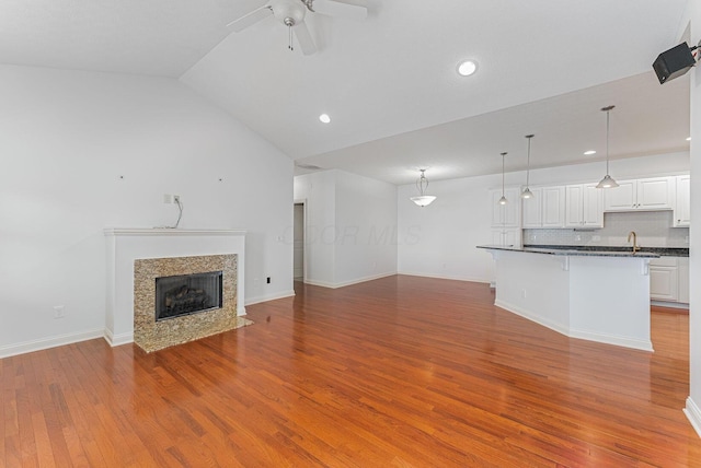 unfurnished living room with ceiling fan, sink, light hardwood / wood-style flooring, a high end fireplace, and lofted ceiling