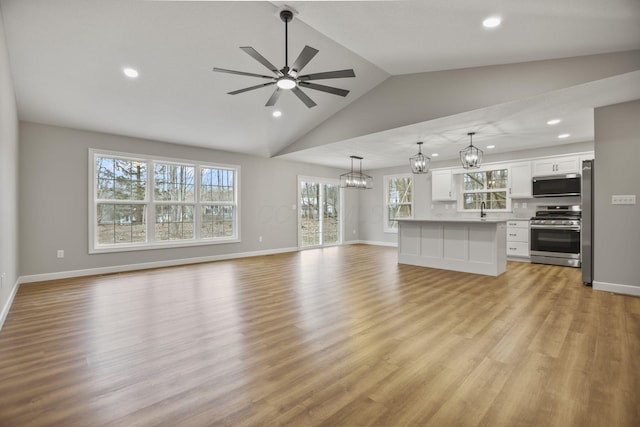 unfurnished living room featuring sink, ceiling fan with notable chandelier, light hardwood / wood-style floors, and vaulted ceiling