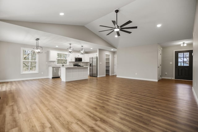 unfurnished living room featuring ceiling fan with notable chandelier, sink, light hardwood / wood-style flooring, and vaulted ceiling