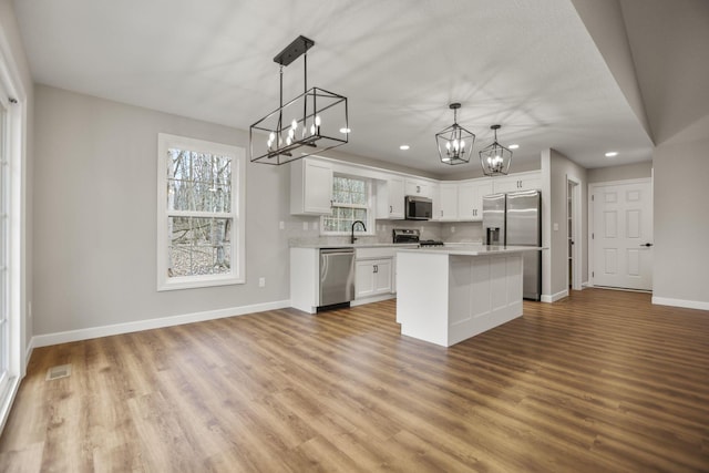 kitchen featuring pendant lighting, sink, appliances with stainless steel finishes, a kitchen island, and white cabinetry