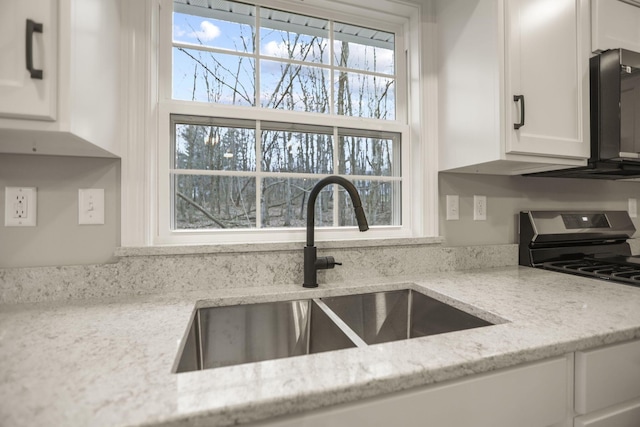 kitchen with light stone countertops, a wealth of natural light, gas stove, sink, and white cabinetry