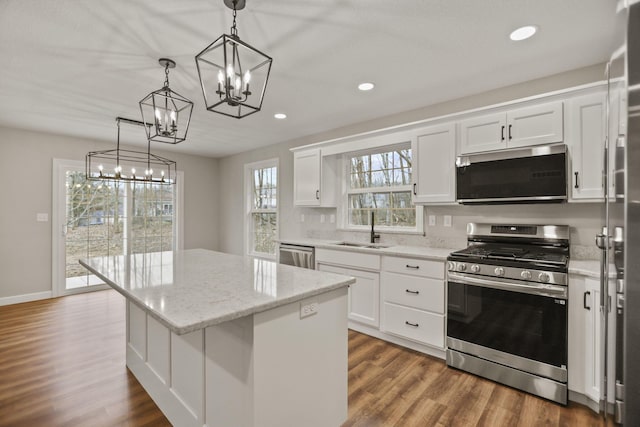 kitchen with white cabinetry, sink, hanging light fixtures, stainless steel appliances, and a kitchen island