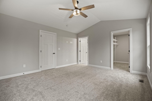 unfurnished bedroom with ceiling fan, a spacious closet, vaulted ceiling, light carpet, and a closet