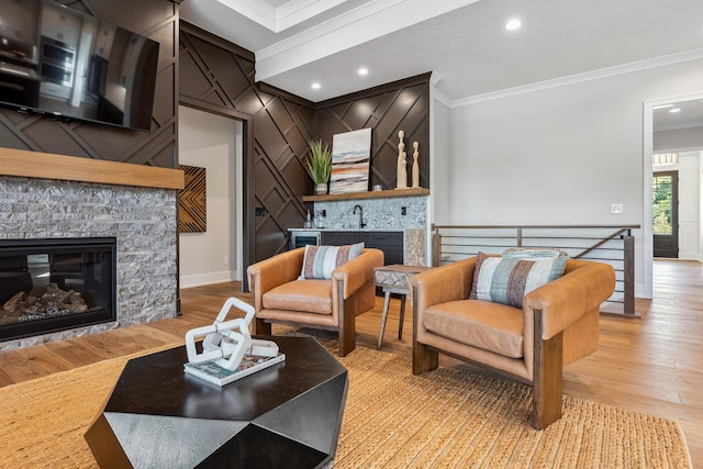 living room with light hardwood / wood-style floors, a stone fireplace, ornamental molding, and sink