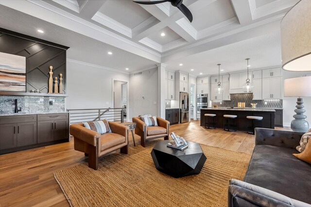 living room featuring beam ceiling, light hardwood / wood-style floors, ornamental molding, and coffered ceiling