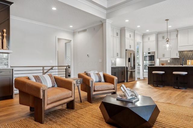 living room featuring light wood-type flooring, crown molding, and sink