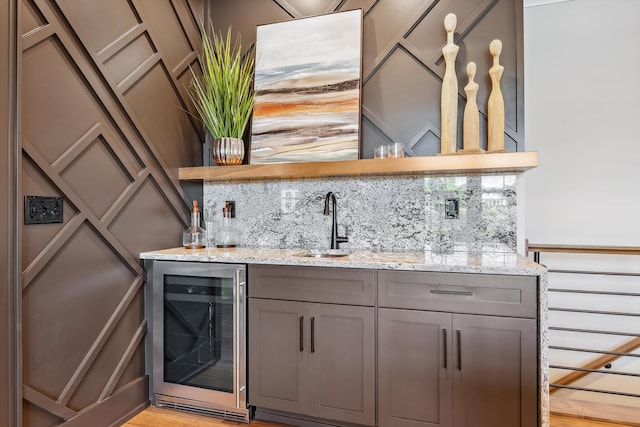 bar featuring decorative backsplash, light stone countertops, beverage cooler, and light hardwood / wood-style floors