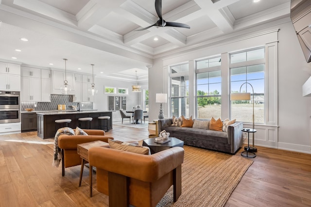 living room with light wood-type flooring, coffered ceiling, ceiling fan, crown molding, and beam ceiling