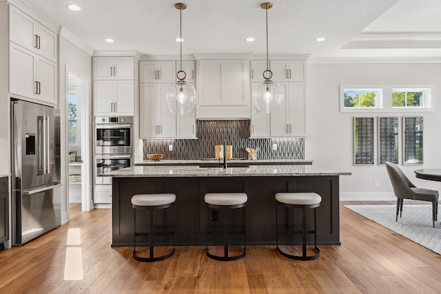 kitchen with stainless steel appliances, white cabinetry, and a kitchen island with sink