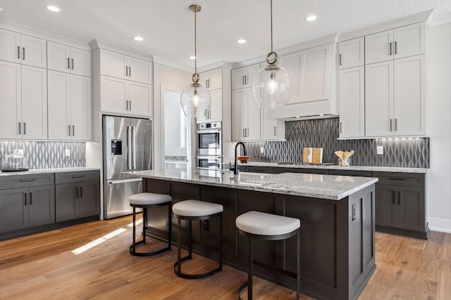 kitchen with appliances with stainless steel finishes, pendant lighting, light hardwood / wood-style flooring, white cabinets, and an island with sink