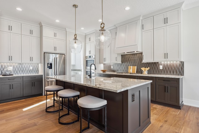 kitchen with white cabinetry, a center island with sink, stainless steel appliances, and decorative light fixtures