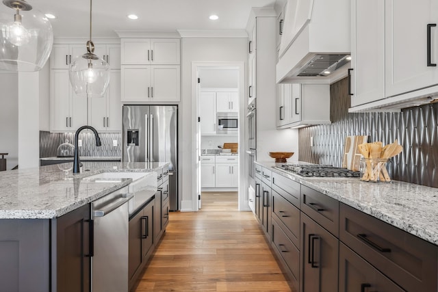 kitchen featuring tasteful backsplash, custom exhaust hood, pendant lighting, white cabinets, and light hardwood / wood-style floors