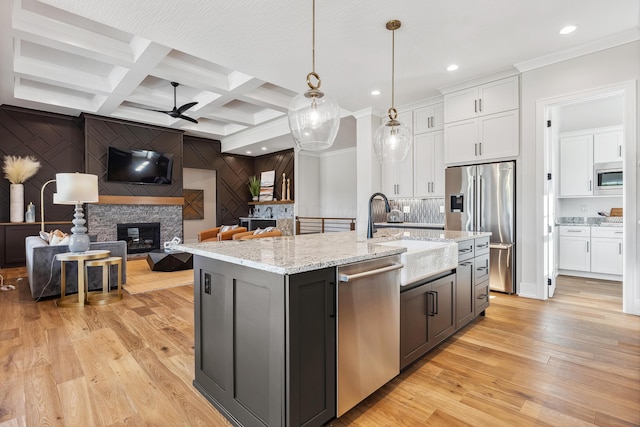 kitchen with stainless steel appliances, ceiling fan, pendant lighting, white cabinets, and an island with sink