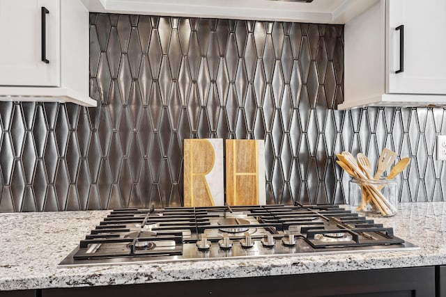 room details featuring stainless steel gas stovetop, light stone countertops, white cabinetry, and backsplash