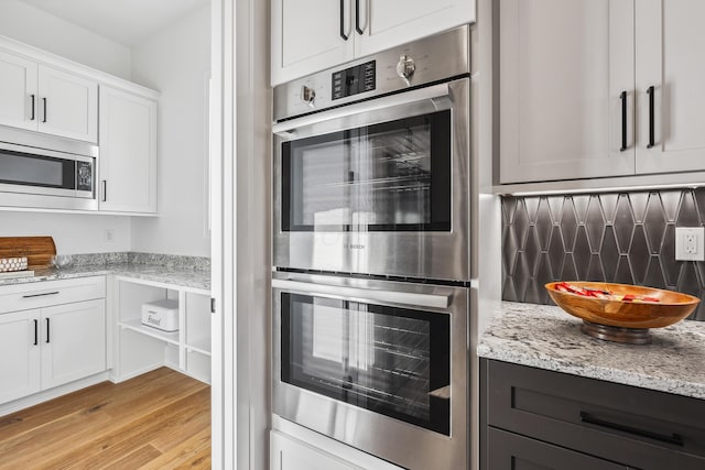 kitchen with light stone counters, white cabinets, light wood-type flooring, and appliances with stainless steel finishes