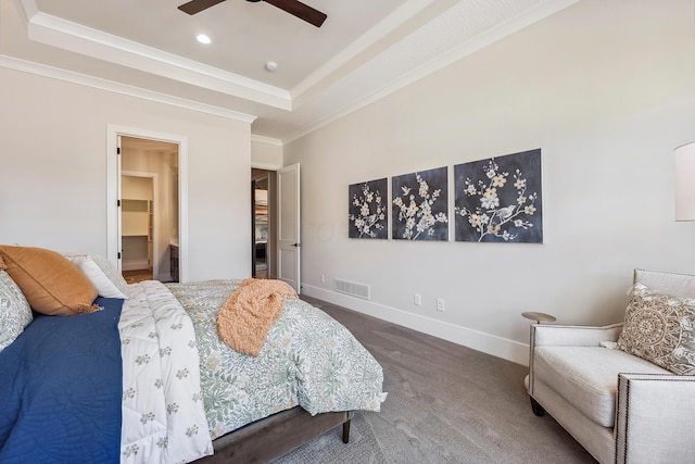 carpeted bedroom with a tray ceiling, a walk in closet, ceiling fan, and ornamental molding