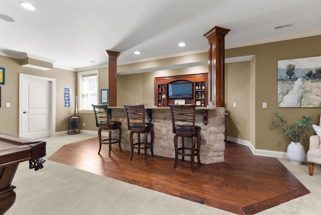 bar with decorative columns, ornamental molding, and wood-type flooring