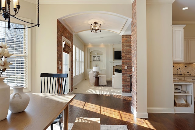 hall featuring built in features, wood-type flooring, ornamental molding, and a chandelier