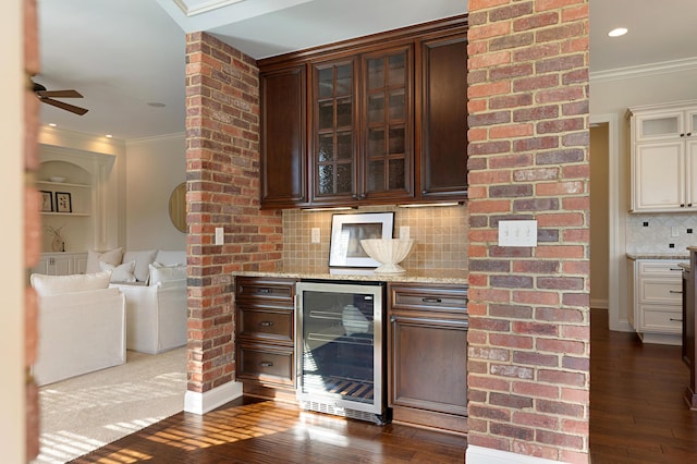 bar featuring hardwood / wood-style flooring, crown molding, backsplash, wine cooler, and dark brown cabinetry