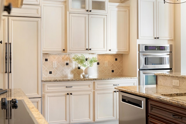 kitchen with light stone countertops, backsplash, stainless steel appliances, and cream cabinetry