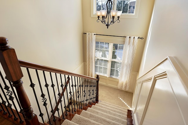 staircase with a chandelier and carpet floors