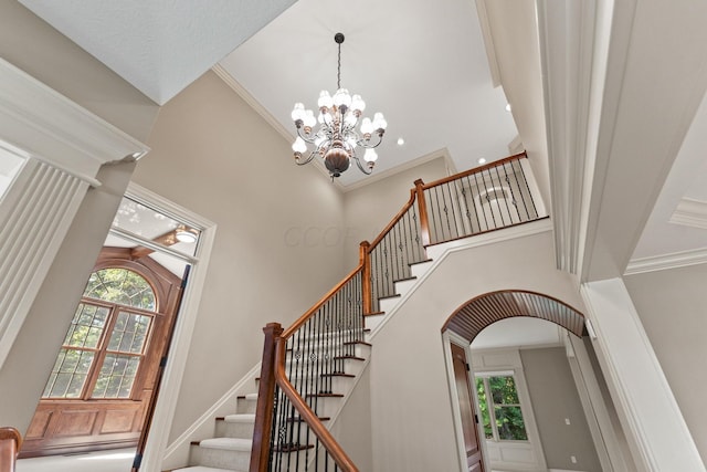 stairway with a notable chandelier, a towering ceiling, and ornamental molding