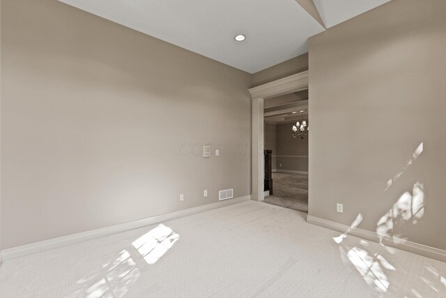 spare room featuring light carpet and a chandelier