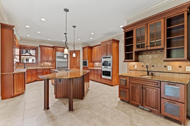 kitchen featuring light stone countertops, crown molding, sink, built in appliances, and an island with sink