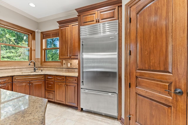 kitchen with sink, built in refrigerator, light stone countertops, tasteful backsplash, and light tile patterned flooring