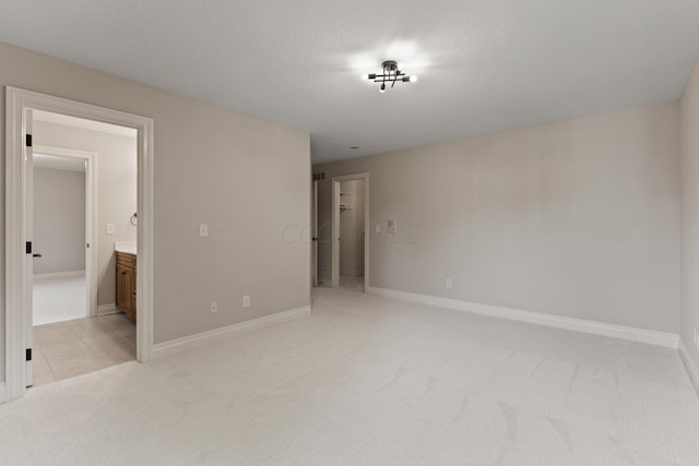 unfurnished bedroom featuring a textured ceiling, connected bathroom, and light colored carpet