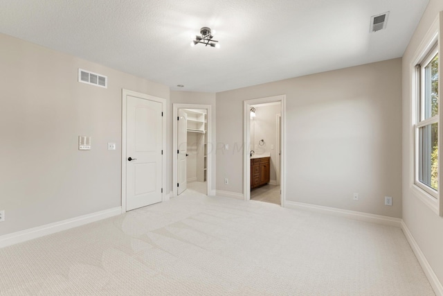 unfurnished bedroom featuring a closet, a walk in closet, light carpet, and ensuite bath