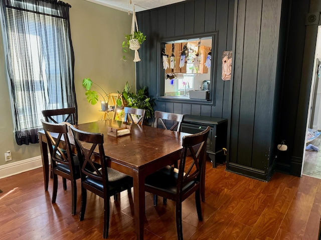 dining area with hardwood / wood-style floors, ornamental molding, and wooden walls