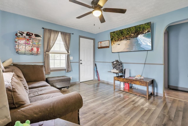 living room with ceiling fan, a textured ceiling, and light wood-type flooring