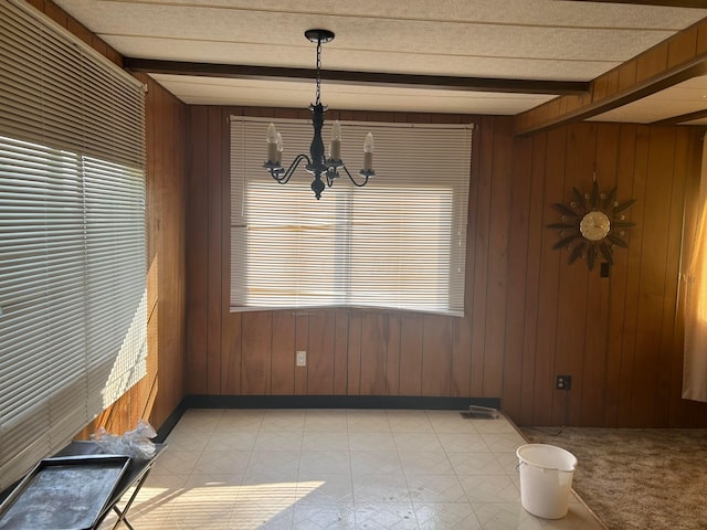 unfurnished dining area with wooden walls, a chandelier, and beamed ceiling