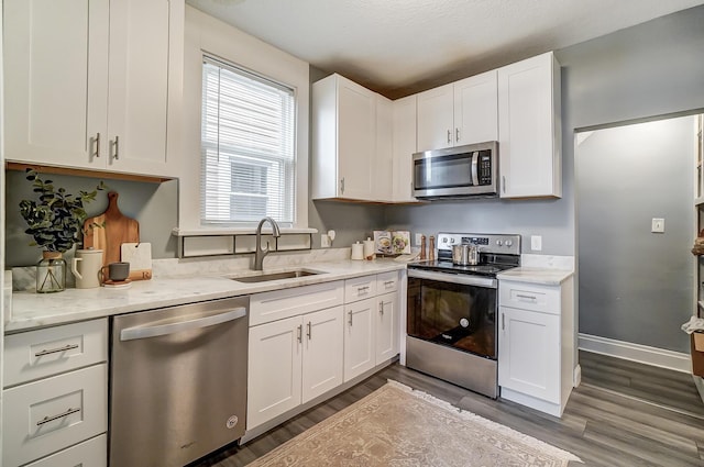 kitchen featuring light stone countertops, appliances with stainless steel finishes, dark wood-type flooring, sink, and white cabinetry