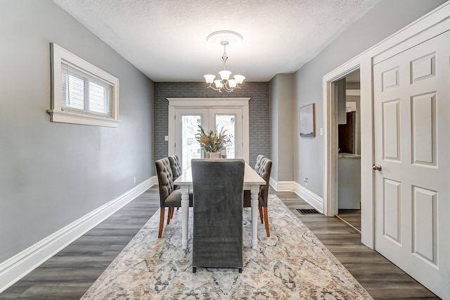 dining room with brick wall, dark wood-type flooring, a textured ceiling, and an inviting chandelier