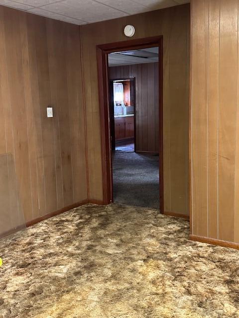 hall with dark colored carpet and wooden walls