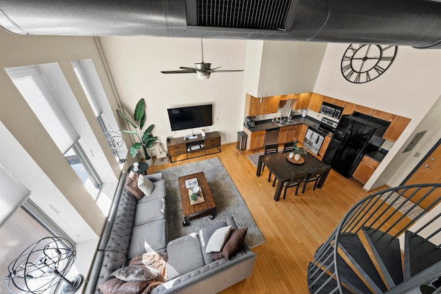 living room with sink, a towering ceiling, ceiling fan, and light wood-type flooring