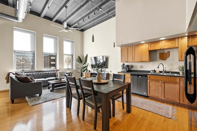 kitchen with a towering ceiling, dishwasher, sink, and light hardwood / wood-style flooring