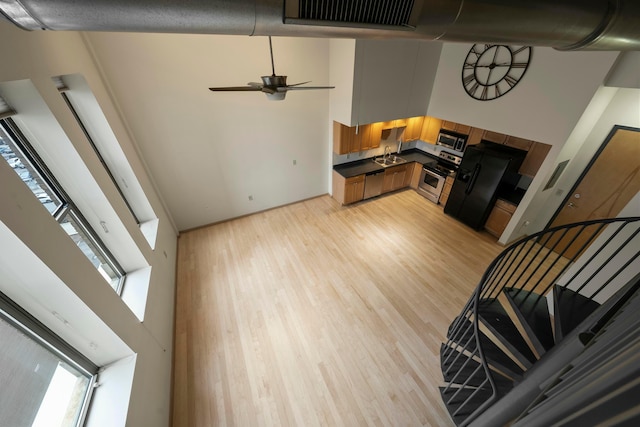 kitchen with sink, light wood-type flooring, a towering ceiling, ceiling fan, and stainless steel appliances