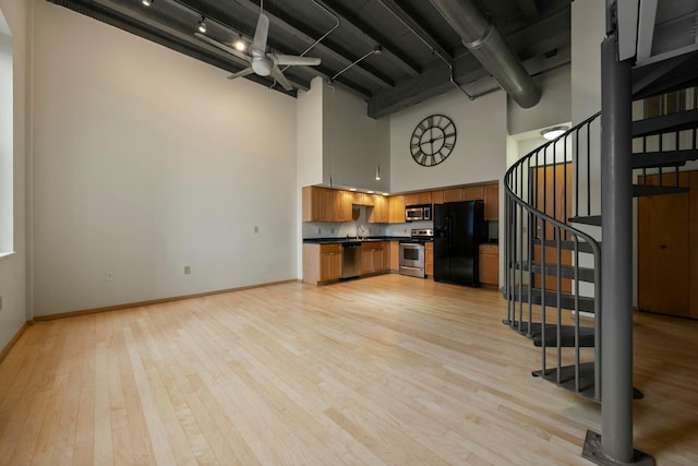 unfurnished living room featuring a high ceiling, light wood-type flooring, sink, and ceiling fan