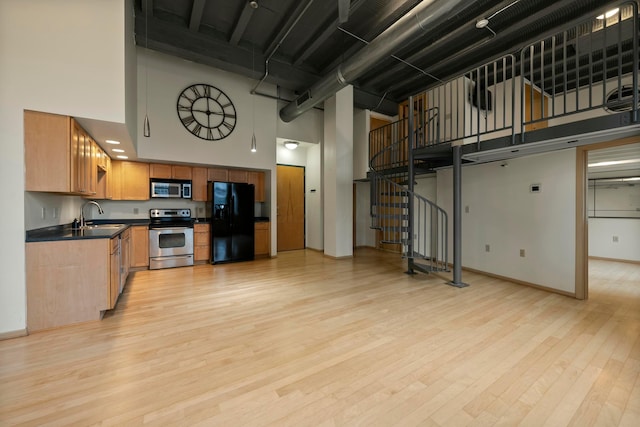 kitchen featuring a towering ceiling, stainless steel appliances, light hardwood / wood-style floors, and sink